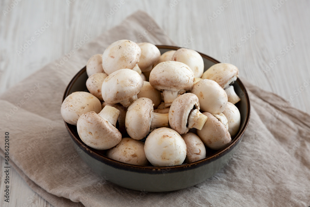 Raw White Champignon Mushrooms in a Bowl on a white wooden background, side view. Raw White Champignon Mushrooms in a Bowl on a white wooden background, side view.