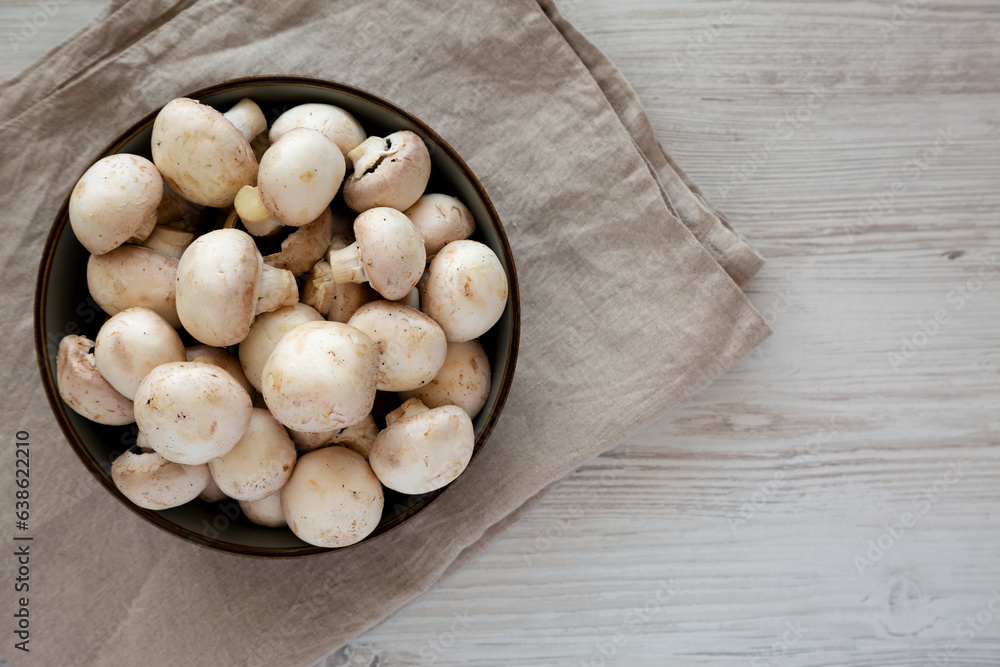 Raw White Champignon Mushrooms in a Bowl on a white wooden background, top view. Raw White Champignon Mushrooms in a Bowl on a white wooden background, top view.