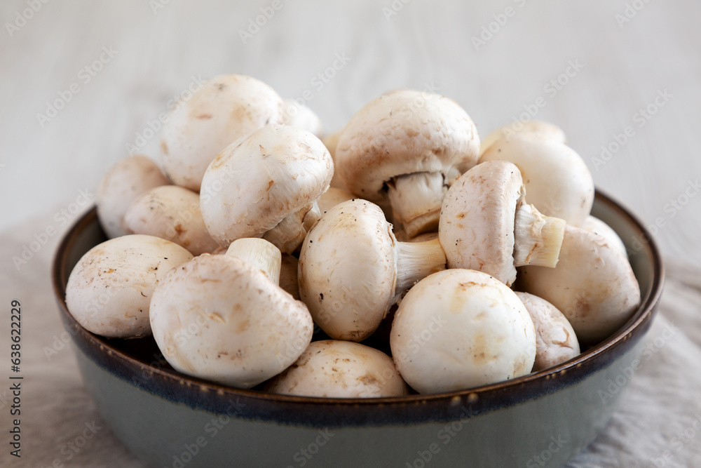 Raw White Champignon Mushrooms in a Bowl on a white wooden background, side view. Close-up. Raw White Champignon Mushrooms in a Bowl on a white wooden background, side view. Close-up.