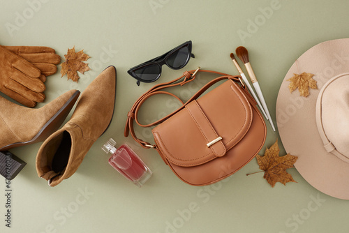 Step into fall\'s embrace with confidence and style. Top view composition of trendy hat, cozy boots, eyewear, handbag, cosmetic brushes, perfume, dry autumn leaves on light green background
