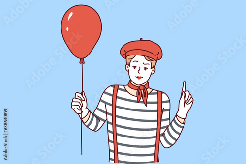 Mime man holding red balloon and pointing finger up, participating in pageant or circus. Mime guy with white face, dressed in long-haired t-shirt and getting ready to make audience laugh