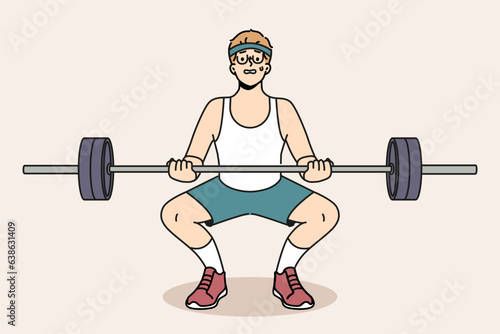 Man with barbell goes in for sports in gym, wanting to have beautiful figure and healthy body. Guy novice bodybuilder squats with barbell in hands and needs help of fitness trainer.