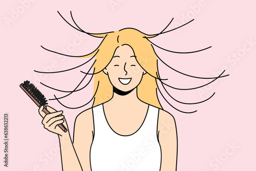 Woman combs hair and smiles, seeing effect of static magnetization of hairstyle. Funny young blonde girl takes care of own hair getting ready for date and laughing feeling surge of positive emotions