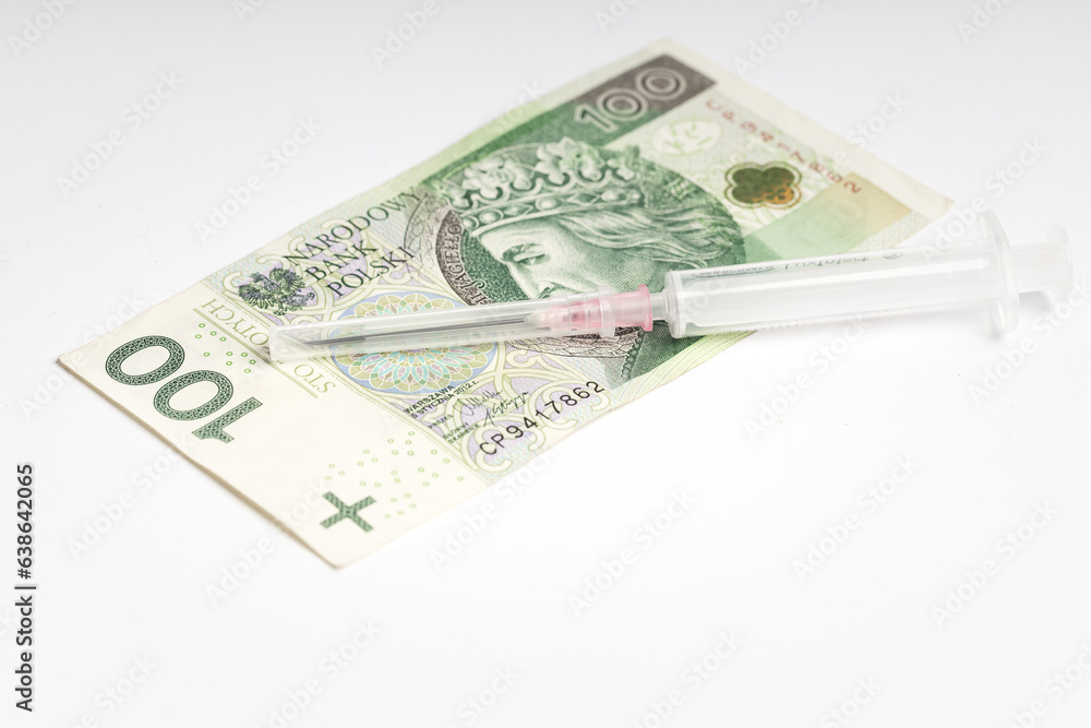 One hundred Polish zlotys lying on a white background, next to a syringe with a needle (selective focus) One hundred Polish zlotys lying on a white background, next to a syringe with a needle (selective focus)