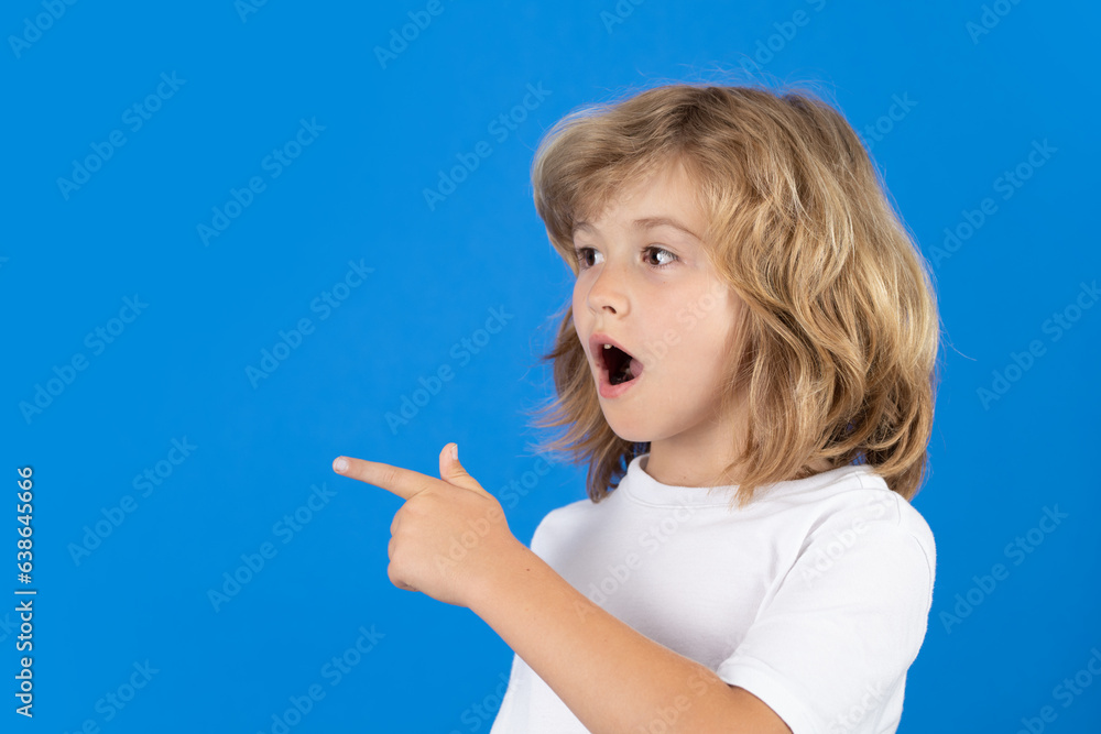 Surprised child looking away, pointing finger on isolated studio background. Shocked kid pointing to copyspace, showing promo offers, points away. Excited emotions, shock, omg and wow expression. Surprised child looking away, pointing finger on isolated studio background. Shocked kid pointing to copyspace, showing promo offers, points away. Excited emotions, shock, omg and wow expression.