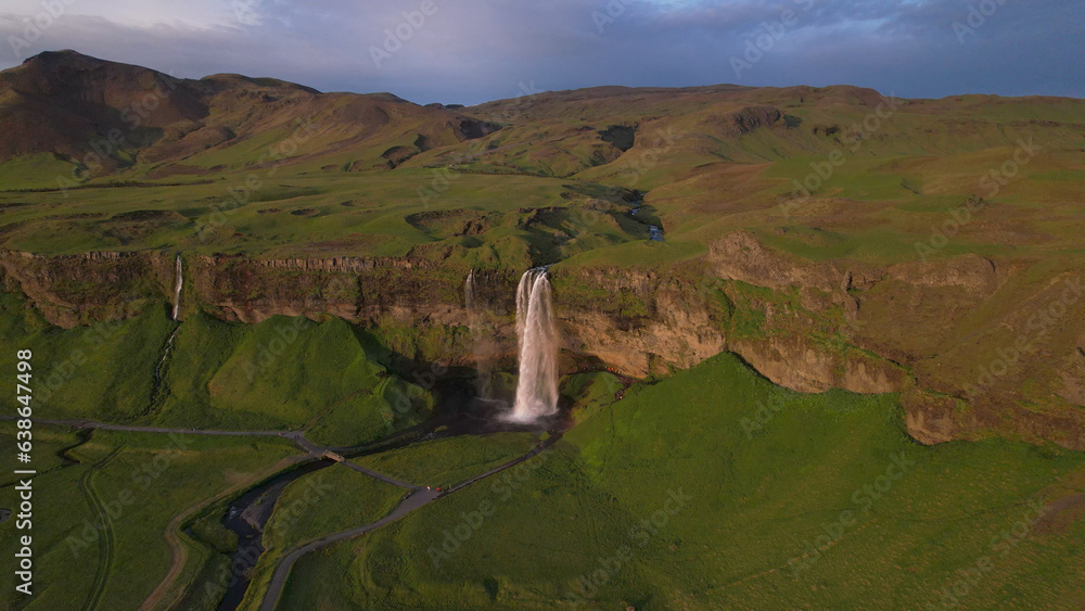 Naklejka premium The Seljalandsfoss waterfall on the south coast of Iceland bathed in the otherworldly light of the midnight sun. The waterfall drops 60 meters and is part of the Seljalands River.