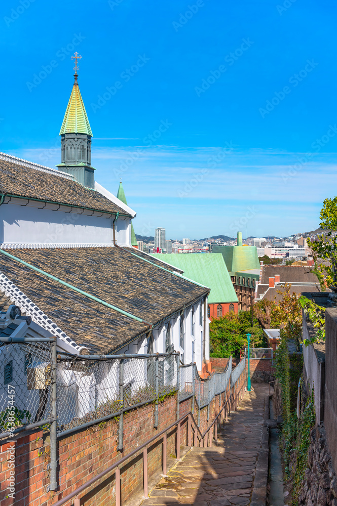 Obraz premium Narrow slope of cobble stairs Kinenzaka going down along the Japanese shikkui plaster walls of the Basilica of the Twenty-Six Holy Martyrs of Japan called Ōura Church in the Nagasaki city of Kyushu.