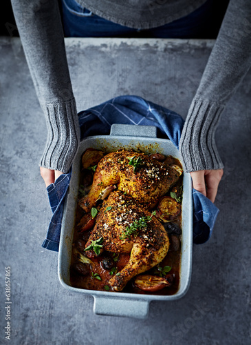 Woman hands holding a ceramik dish with oven-baked chicken legs. Top view. Home cooking concept