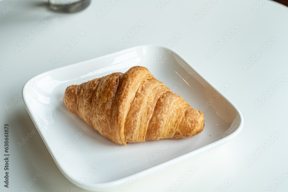 Croissant bread in a white plate lies on a white table Croissant bread in a white plate lies on a white table