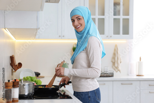 Muslim woman cooking dish in frying pan on cooktop indoors