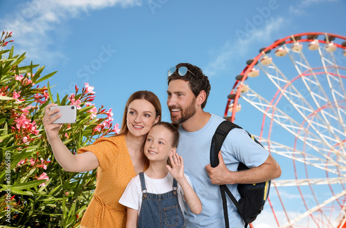Happy family with child taking selfie near observation wheel outdoors