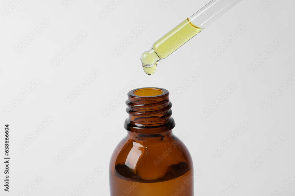 Dripping cosmetic oil from pipette into bottle on white background, closeup Dripping cosmetic oil from pipette into bottle on white background, closeup