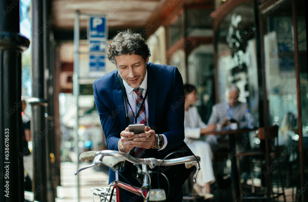Young caucasian businessman using a smart phone while commuting to work with his bicycle Young caucasian businessman using a smart phone while commuting to work with his bicycle