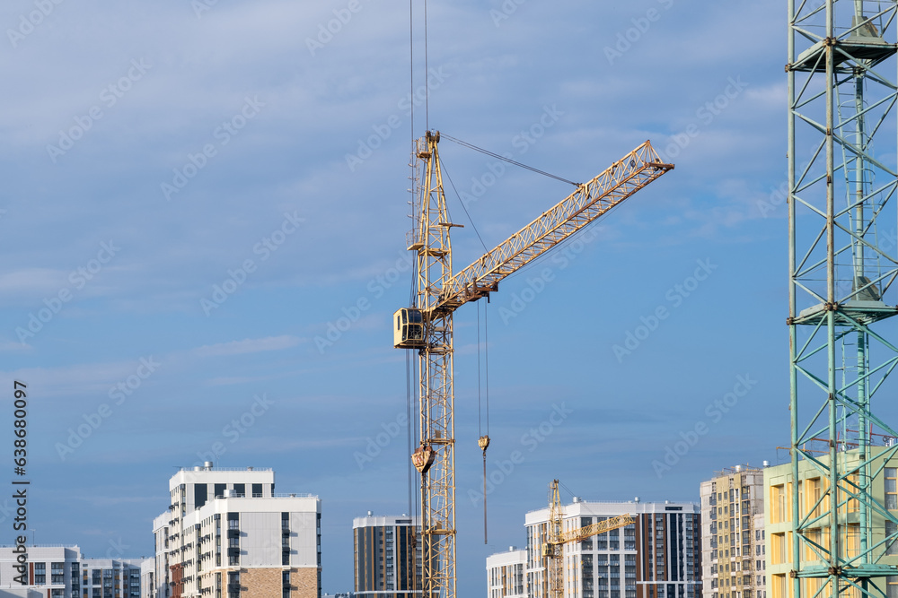 A crane and a building under construction against a blue sky background. Builders work on large construction sites, and there are many cranes working in the field of new construction.