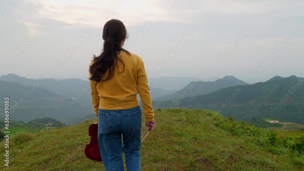 young woman holds a violin and walks to the edge of a windy mountaintop young woman holds a violin and walks to the edge of a windy mountaintop