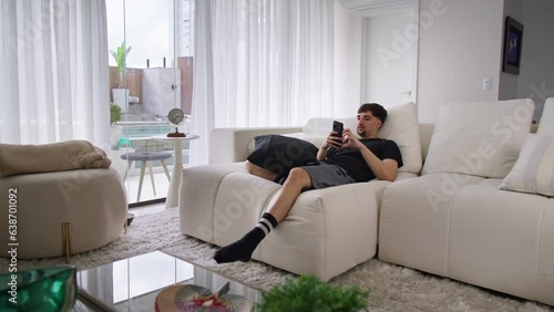 Handsome Caucasian Man Using Smartphone in Cozy Living Room at Home. Man Resting on Comfortable Sofa.Checking Videos on Social Networks and Browsing the Internet and Having Fun.