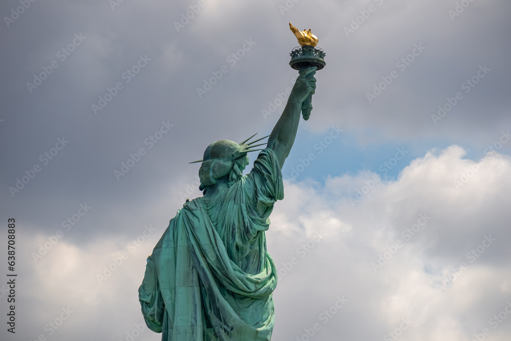Fototapeta premium A close up on an iconic representation of freedom and independence, the Statue of Liberty with flaming torch on Liberty Island. The Lady on a Pedestal is surrounded by clouds. American history.