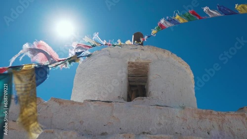 Slow motion shot of Buddhist prayer flags waving on old monastery, stupa in Zanskar, Ladakh, India. Monastery view during blue sunny day of summer. 