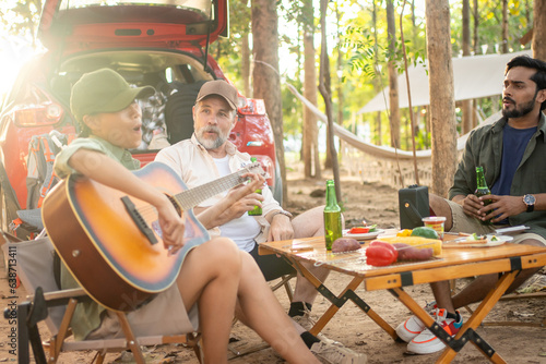 Group tourists drinking beer-alcohol and play guitar together with enjoy and happiness in Summer while camping