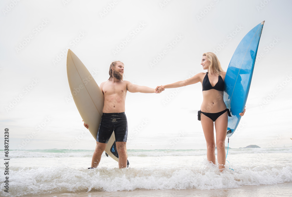 Couple of surfers holding hands and looking at each other on beach