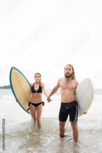 Couple of surfers holding hands and looking at each other on beach