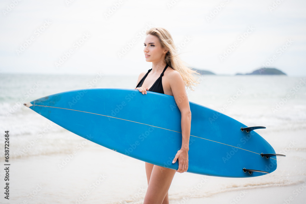 Surfer girl with her surfboard on the beach.