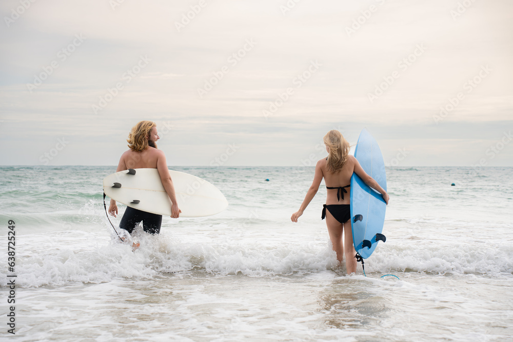 Young man and woman holding surfboards ready to walk into the sea to surf.