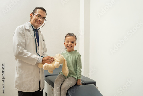 doctor using stethoscope listening teddy bear heartbeat. pediatrician building confidence on child. kid smiling at doctor's office. Doctor and girl smiling looking at camera