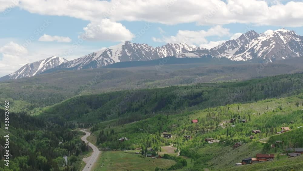 Closeup aerial view pan right of beautiful Colorado mountain range with snow capped peaks on a sunny, blue sky day in the summer with green fields, trees, and mountain homes Closeup aerial view pan right of beautiful Colorado mountain range with snow capped peaks on a sunny, blue sky day in the summer with green fields, trees, and mountain homes