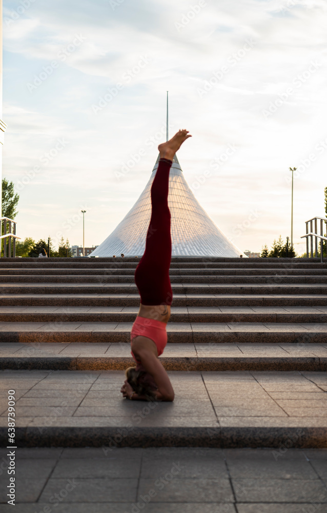 Portrait of a mature woman, 59 years old, doing yoga on a city street. Woman doing a headstand.