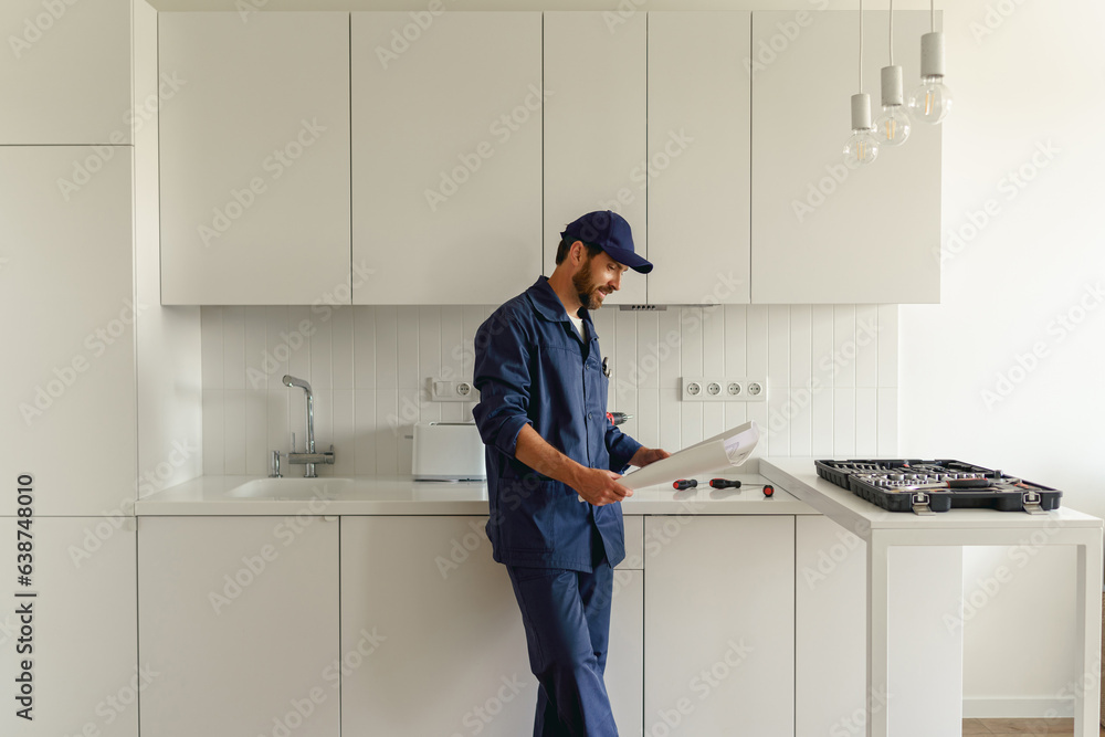 Handyman in uniform standing on kitchen with home plan before starting work Handyman in uniform standing on kitchen with home plan before starting work