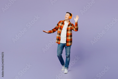 Full body young happy man he wears checkered shirt white t-shirt casual clothes listen to music in headphones raise up hands dance isolated on plain pastel light purple background. Lifestyle concept.