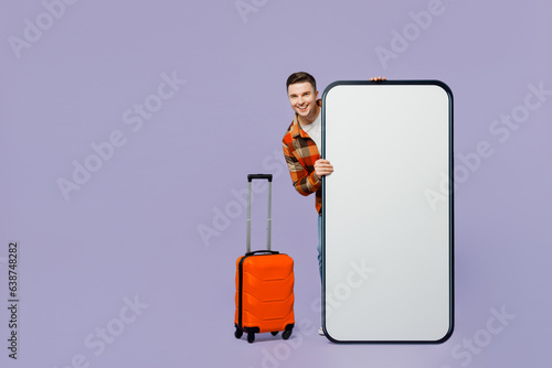 Traveler man hold suitcase big huge blank screen mobile cell phone isolated on plain pastel purple background. Tourist travel abroad in free spare time rest getaway. Air flight trip journey concept. #638748282