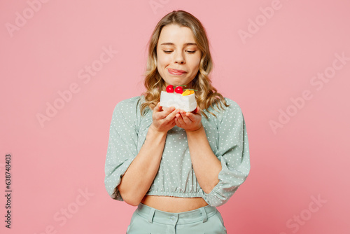 Young smiling satisfied fun happy woman she wear casual clothes look at tasty piece of seet cake dessert, lick lips isolated on plain pastel light pink background studio portrait. Lifestyle concept. photo