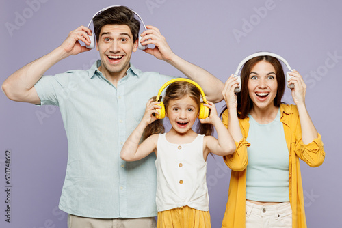 Young fun surprised parents mom dad with child kid daughter girl 6 years old wear blue yellow casual clothes listen to music in headphones dance isolated on plain purple background Family day concept