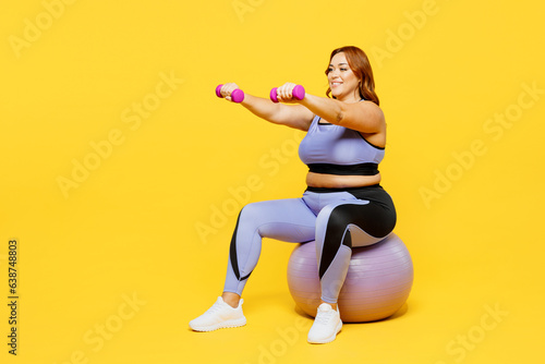 Full body young chubby plus size big fat fit woman wear blue top warm up train sit on fit ball hold dumbbell raise up hands isolated on plain yellow background studio home gym Workout sport concept photo