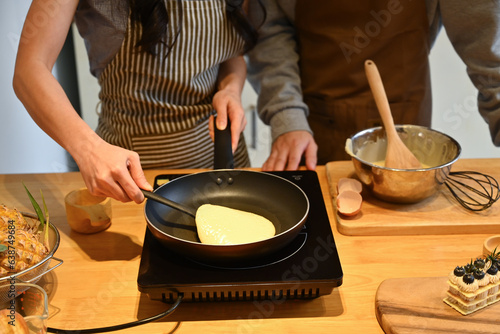 Cropped shot of young couple making pancakes on frying pan, preparing breakfast in kitchen
