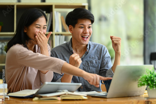 Overjoyed college students looking at laptop screen celebrating success, exam results together