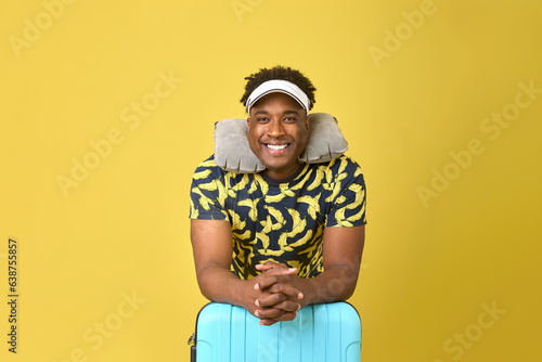 Billede på lærred Cute African-American traveler standing smiling with a suitcase and a pillow around his neck on a yellow background
