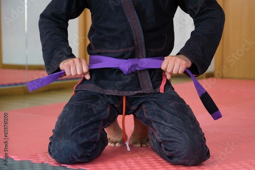 Cropped shot of an unrecognizable man tying a purple Brazilian Jiu-Jitsu belt. BJJ training. photo