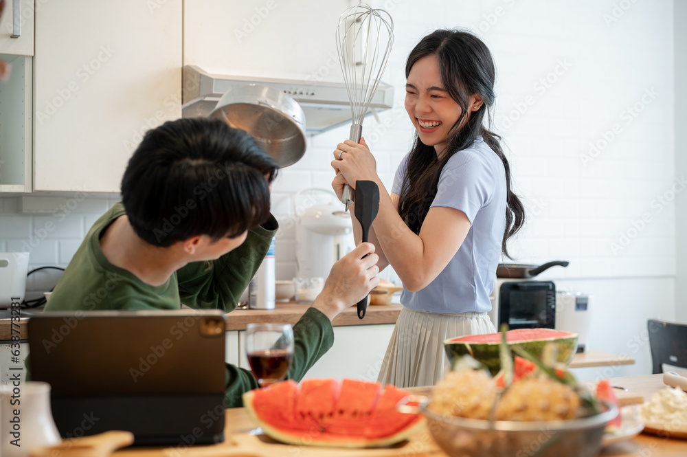 A playful Asian couple is pretending fight with utensils tools and having fun in the kitchen A playful Asian couple is pretending fight with utensils tools and having fun in the kitchen