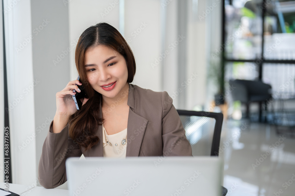 A beautiful Asian businesswoman is looking at her laptop screen while talking on the phone A beautiful Asian businesswoman is looking at her laptop screen while talking on the phone