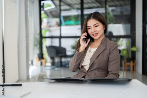 A beautiful Asian businesswoman is looking at details on a document and talking on the phone