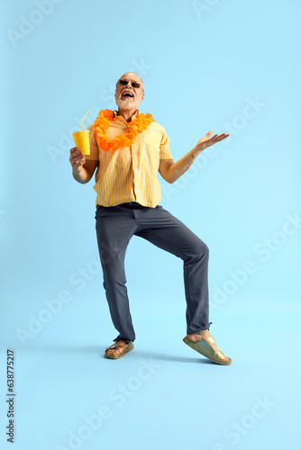 Full-lenght portrait of attractive happy middle-aged grey-head man, stylishly, brightly dressed in summer, holding refreshing cocktail