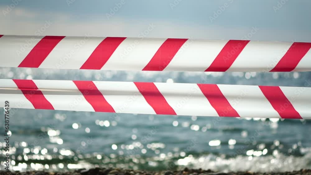 Red white warning tape barrier ribbon swinging in the wind across exotic sea beach background without people. No entry Red White caution tape. No holiday concept, delayed travel, no summer plans Red white warning tape barrier ribbon swinging in the wind across exotic sea beach background without people. No entry Red White caution tape. No holiday concept, delayed travel, no summer plans