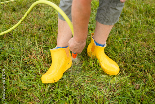 Washing of rubber boots. Close-up of a woman's hands washes yellow rubber boots from mud with a garden hose in the garden after working in the ground