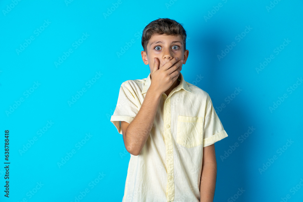 Emotional Beautiful kid boy wearing casual shirt gasps from astonishment, covers opened mouth with palm, looks shocked at camera. Emotional Beautiful kid boy wearing casual shirt gasps from astonishment, covers opened mouth with palm, looks shocked at camera.