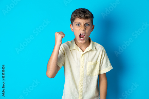 Beautiful kid boy wearing casual shirt angry and mad raising fist frustrated and furious while shouting with anger. Rage and aggressive concept.