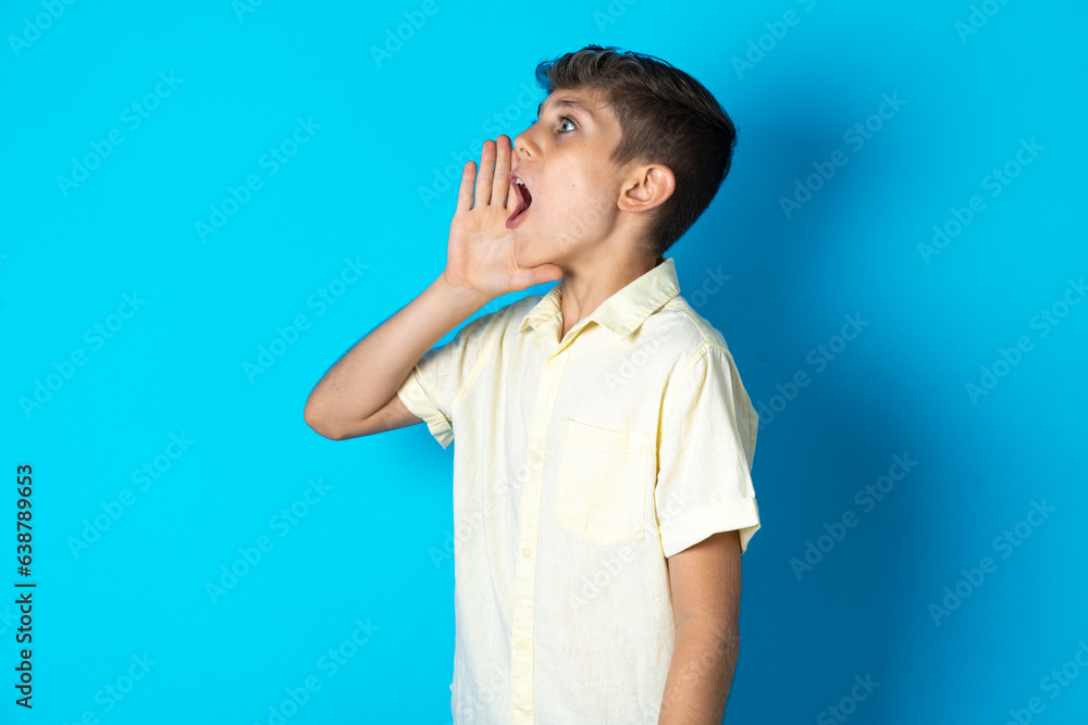 Beautiful kid boy wearing casual shirt shouting and screaming loud to side with hand on mouth. Communication concept. Beautiful kid boy wearing casual shirt shouting and screaming loud to side with hand on mouth. Communication concept.