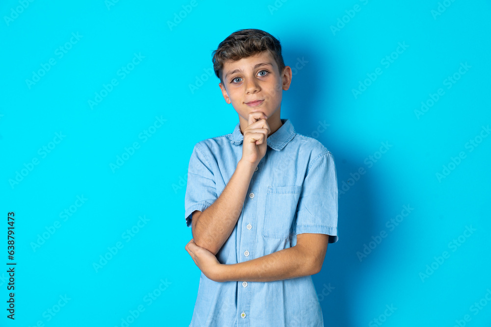 Surprised Beautiful kid boy wearing casual blue shirt makes silence gesture, keeps finger over lips and looks mysterious at camera Surprised Beautiful kid boy wearing casual blue shirt makes silence gesture, keeps finger over lips and looks mysterious at camera